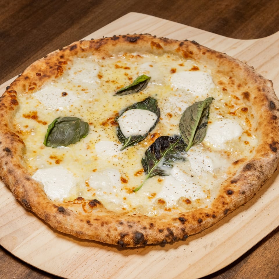CHAR Pizzeria's white pizza with melted mozzarella, fresh basil, and black pepper on a wooden peel.