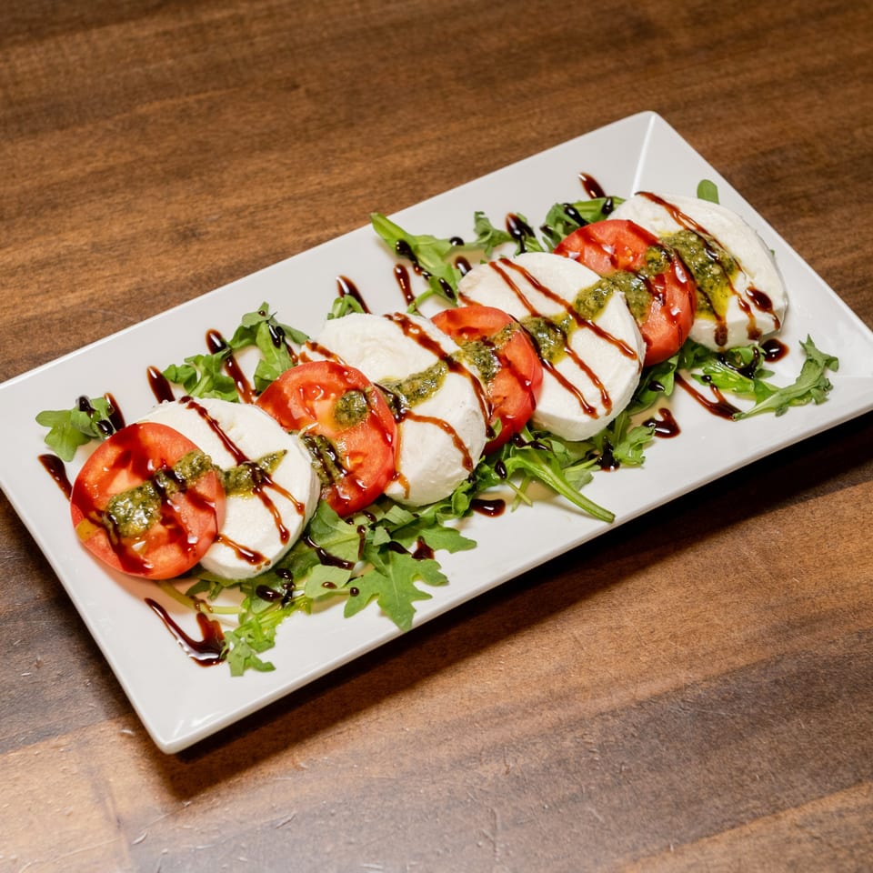 CHAR Pizzeria's Caprese salad with fresh mozzarella, tomatoes, pesto, and balsamic glaze on arugula.