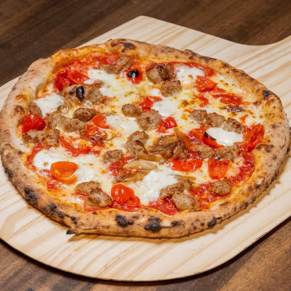 CHAR Pizzeria's sausage and tomato pizza with melted mozzarella on a wooden peel.