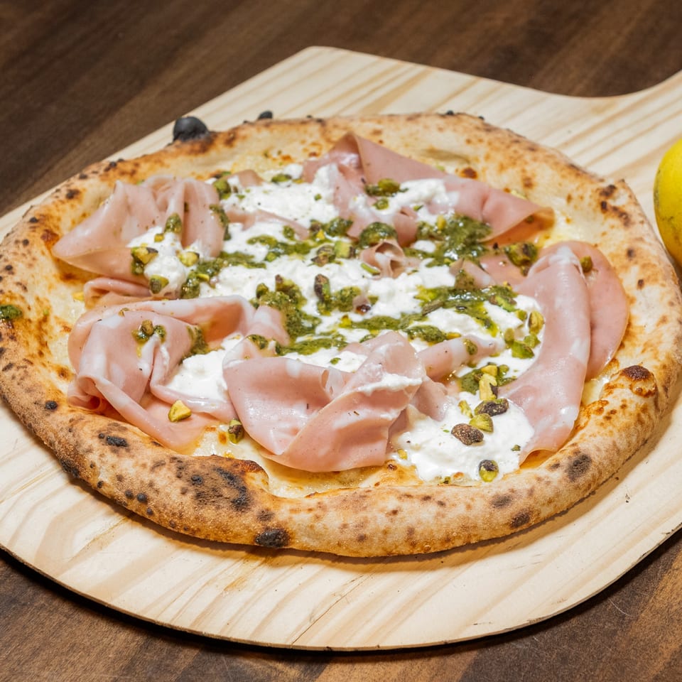 CHAR Pizzeria's pizza with mortadella, burrata, pesto, and pistachios on a wooden peel.