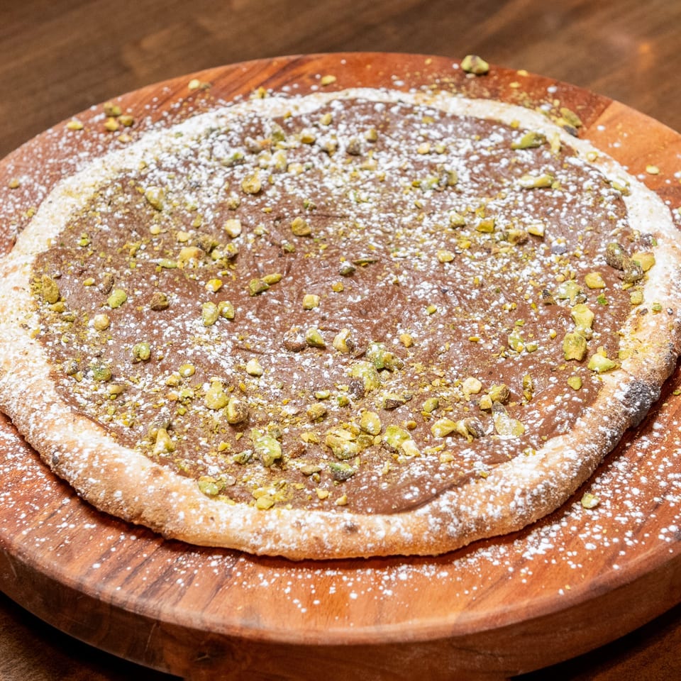CHAR Pizzeria's dessert pizza, topped with chocolate spread, powdered sugar, and chopped pistachios.