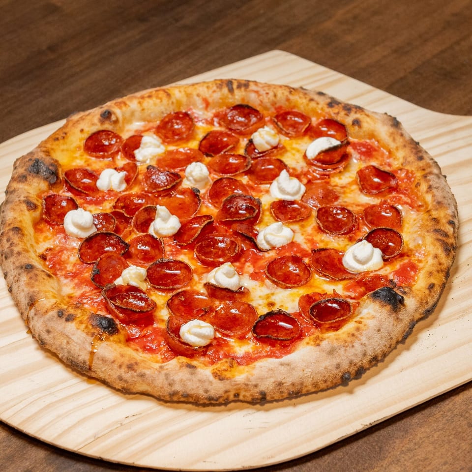 A CHAR Pizzeria pepperoni pizza with dollops of ricotta cheese on a wooden pizza peel.